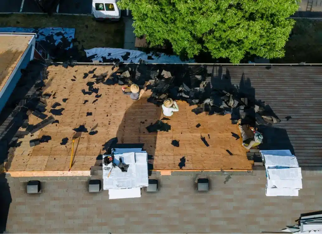 A group of construction workers install new shingles on a low pitched roof. 