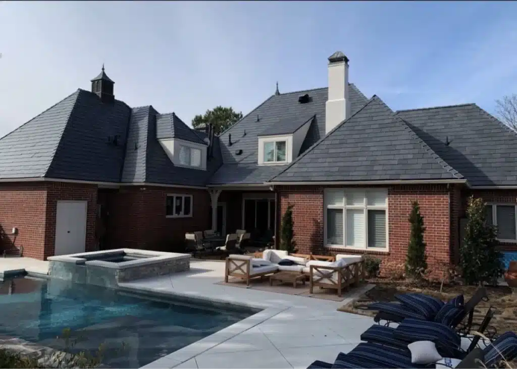A house with dark roof shingles and a pool in front of it