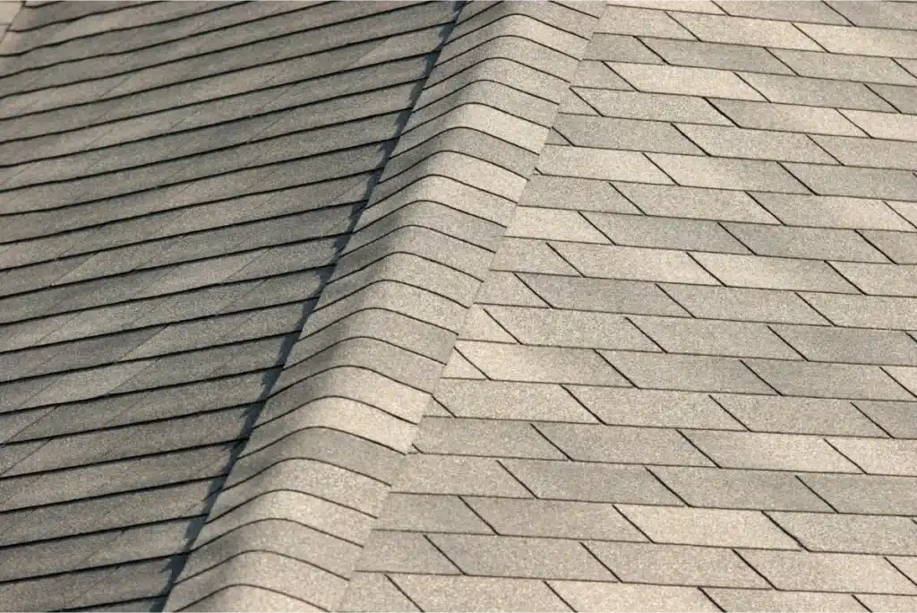 Close-up view of a roof ridge with neatly aligned gray asphalt shingles, showcasing the intersection of two roof sections.