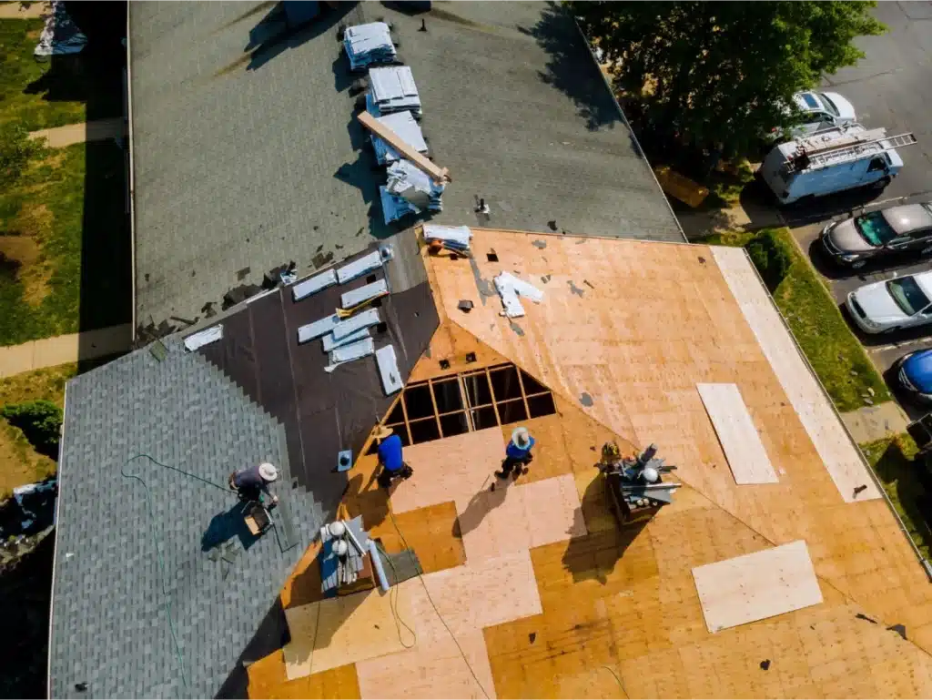 Aerial view of a large roofing project with multiple workers installing new plywood and shingles on a residential roof.