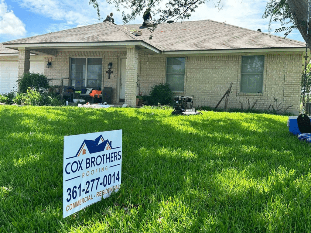 Cox Brothers Roofing sign in front yard with workers on roof.